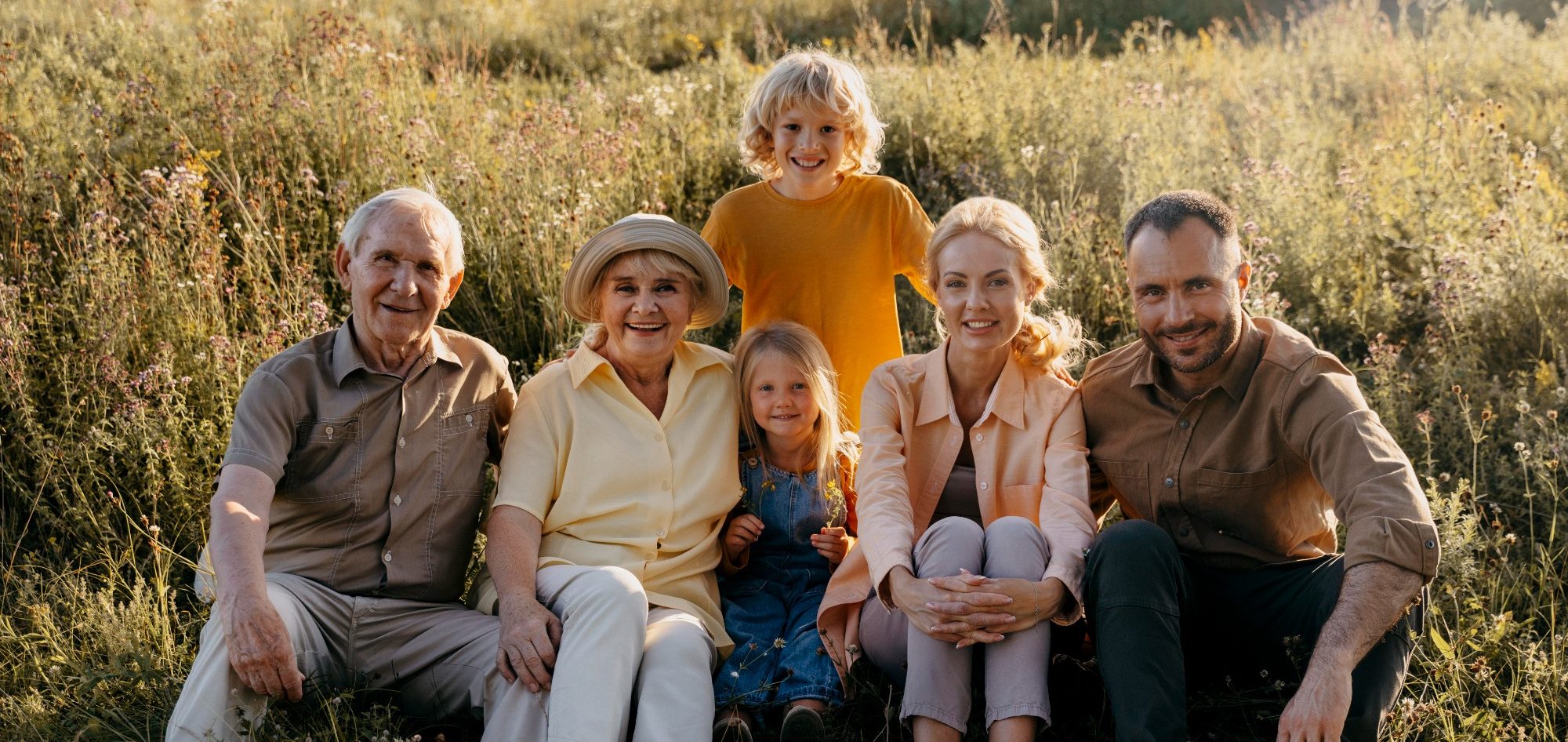 Craniosacral und osteopathische Therapie für jede Altersgruppe der Familie Familie sitzt auf Wiese, lächelt, umgeben von grünen Pflanzen, sonniges Wetter.